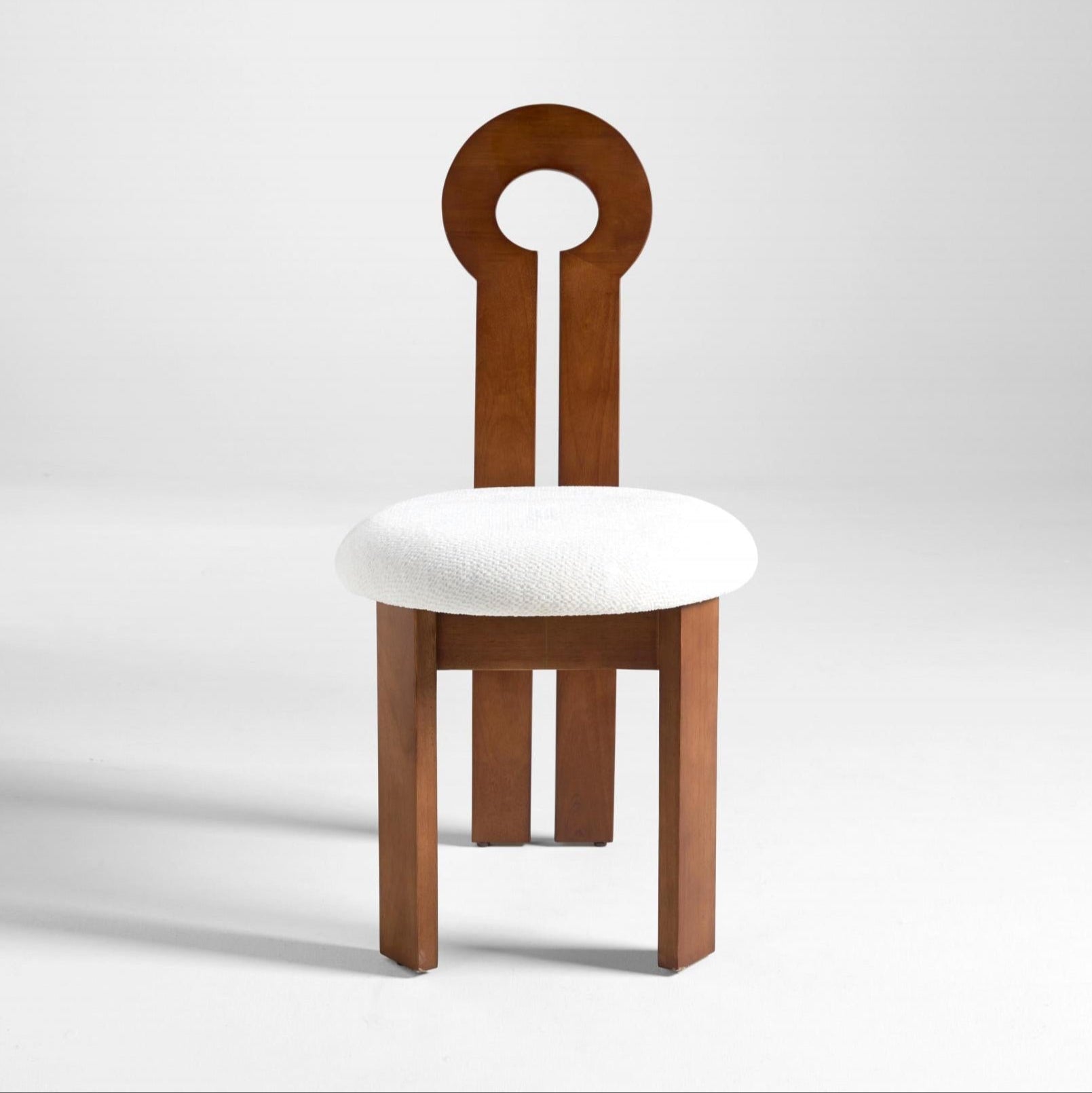 A dining chair with a solid rubber wood frame and a round white upholstered seat, featuring a unique circular design at the top of the backrest.